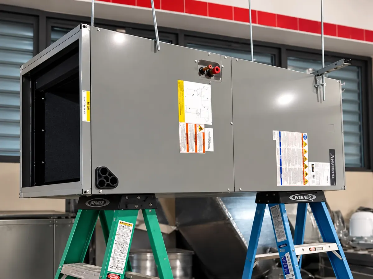 Large gray commercial air handler installed by Arijen, suspended on threaded rods during an installation